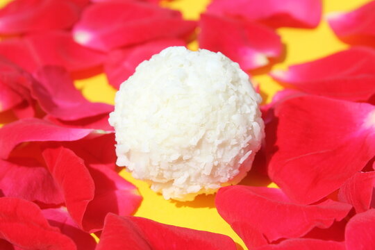 On a yellow background lies a round candy with coconut and red rose petals.
