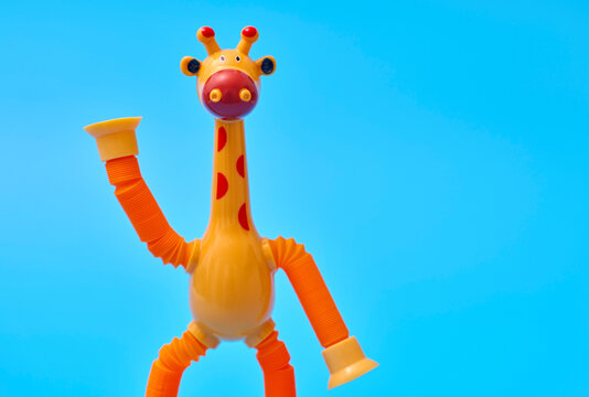 Orange giraffe toy with raised arm greeting on blue background