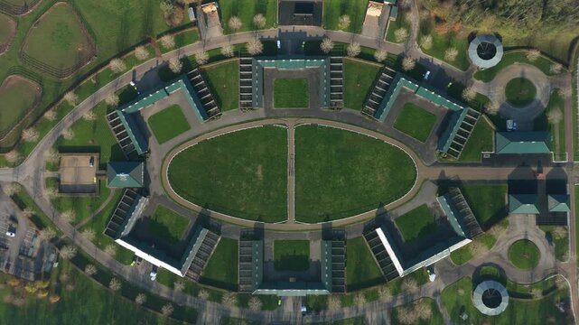 Cinematic drone perspective of the famous Newmarket gallops and elite racing yards in England featuring thoroughbred mares and future champions.