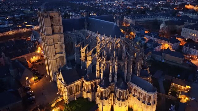 Drone shot advancing toward Saint-Julien Cathedral nave at night in Le Mans, with illuminated Gothic architecture and city lights surrounding. France