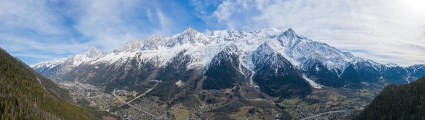 Fototapeta premium Expansive panorama of the Mont Blanc massif towering over the Chamonix valley, with snowy peaks, forested slopes, and a patchwork of villages under a sky streaked with soft clouds.