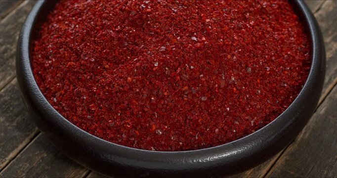 A bowl of gochugaru, Korean red chilli pepper flakes, rotating on a rustic wooden background. 