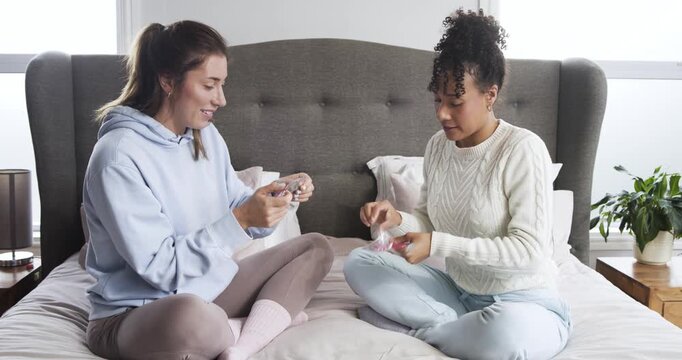 Reaching for skincare sachets, diverse female friends testing and applying eye masks on bed