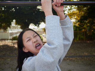 春の昼の公園で楽しく鉄棒で遊んでいる十代の女の子の姿