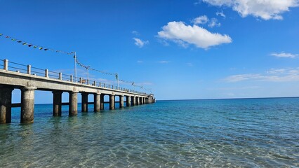 Concrete pier stretching into the clear turquoise waters of the Atlantic Ocean in Porto Santo, Madeira, Portugal, under a bright blue sky with scattered clouds. © Sebastiaan89