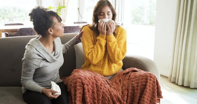 Diverse female friends reading smartphone message and offering tissues while sniffling on gray sofa