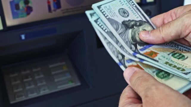 Person's hands count 100 dollar banknotes near ATM machine. A man withdraws cash money. Close up real time motion video.