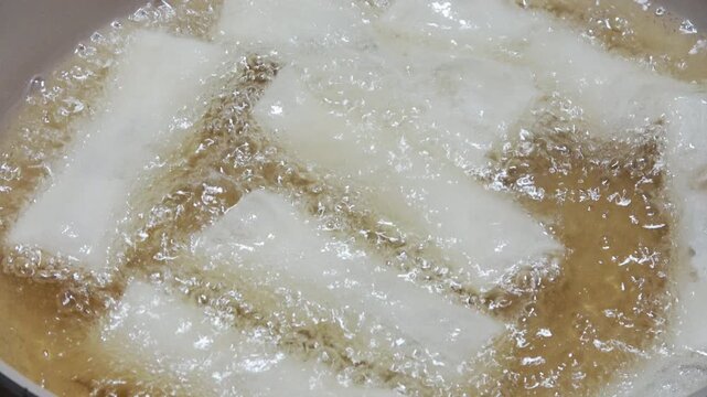 Spring rolls being deep-fried in hot oil.