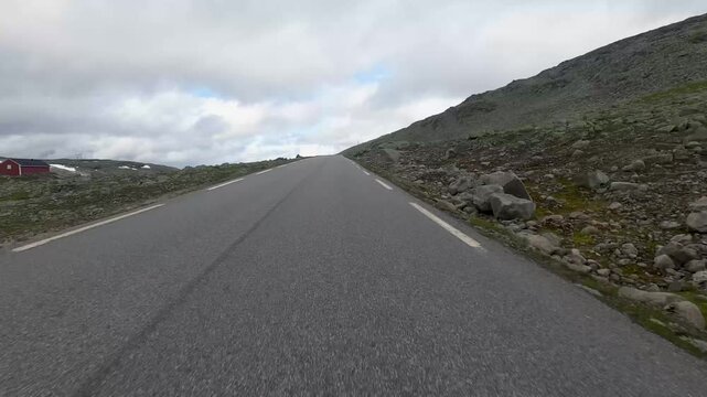POV shot from a moving vehicle on the Bj&oslash;rgavegen road in Nalfarbakkane, Norway, next to a glacial lake with a small cabin. No people