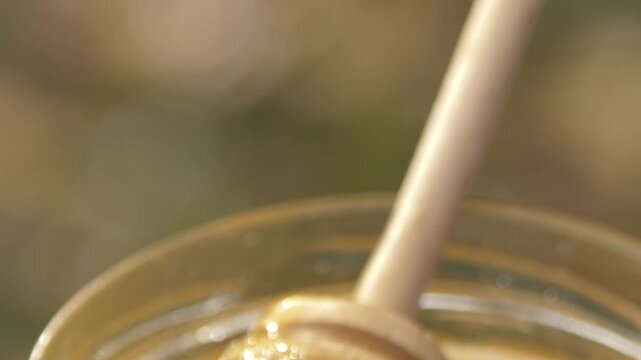 Close-up detailed view of a beekeeper's hand stirring creamy white rapeseed honey in a glass jar at the apiary, showcasing the smooth texture