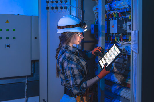 Female electrician audits a switchboard with a tablet schematic. Smart service.