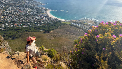 Naklejka premium A hiker enjoys the panoramic view from Lion's Head in Cape Town, South Africa, overlooking the bay of Camps Bay and the surrounding coastline.