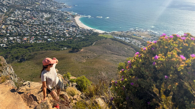 A hiker enjoys the panoramic view from Lion's Head in Cape Town, South Africa, overlooking the bay of Camps Bay and the surrounding coastline.