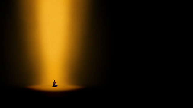 Dramatic artwork. Person meditating under golden spotlight in darkness. Concept of inner light and spiritual focus, resilience in isolation and mental clarity in contrast.