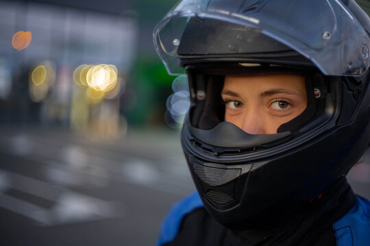 A woman on a motorcycle wearing a helmet and a motorcycle jacket in the evening in the city