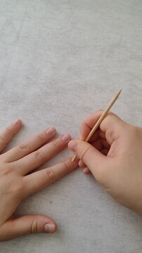 first person vertical video of pushing back cuticle with wooden orange stick. detailed manicure step, precise slow hand movement. clean nail care b-roll for beauty, salon and skincare ads.