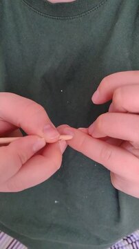 Close-up vertical video of woman pushing back cuticle with wooden orange stick during at-home manicure. Detailed hand care process, natural movement, DIY beauty routine and self care concept.