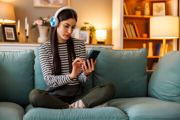 Obraz premium Woman wearing headset having fun using smart phone while relaxing at home