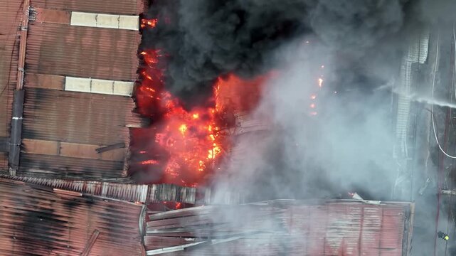 Aerial view fire is burning in a building and firefighters are trying to put it out. The building is in flames and the smoke is billowing out of it