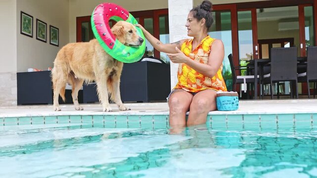 Woman putting a watermelon float on her golden retriever by the pool