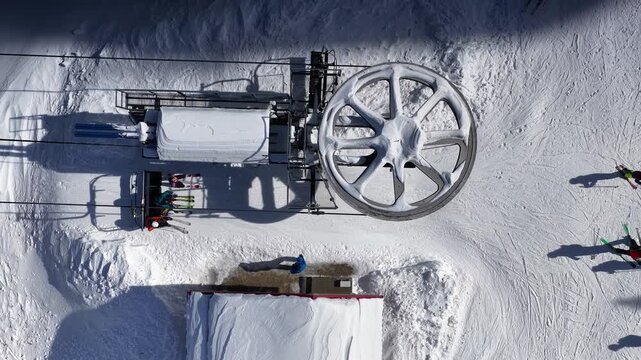 Aerial view over snowy mountain winter forest with chair lift at ski resort. Ski lift cable car top down drone shot. Winter landscape scene with snow covered trees. Outdoor tourism skiing snowboarding