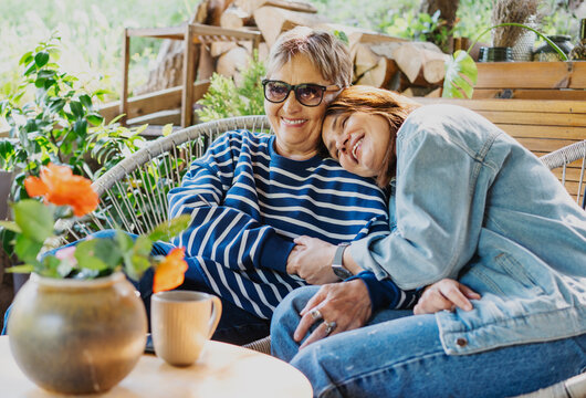 Happy senior mother and adult daughter laughing and hugging on a sunny home terrace