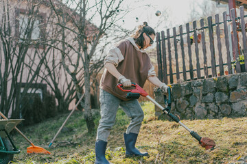 Young woman mowing green grass with lawn mower in the backyard of her countryside house.
