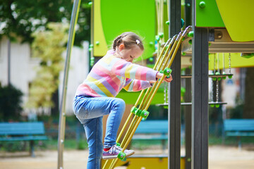 Fototapeta premium Little girl climbing playground equipment using ropes and platforms in a green city park