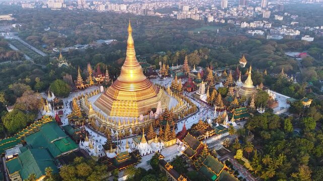 Aerial drone view at Shwedagon Pagoda, a golden stupa, surrounded by lush greenery and urban development in Yangon (Rangun), Myanmar (Burma)., showcasing the city's blend of religious and modern life.