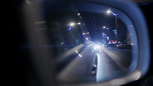 Close up of a side mirror at night with bright headlights from a car behind creating lens flare