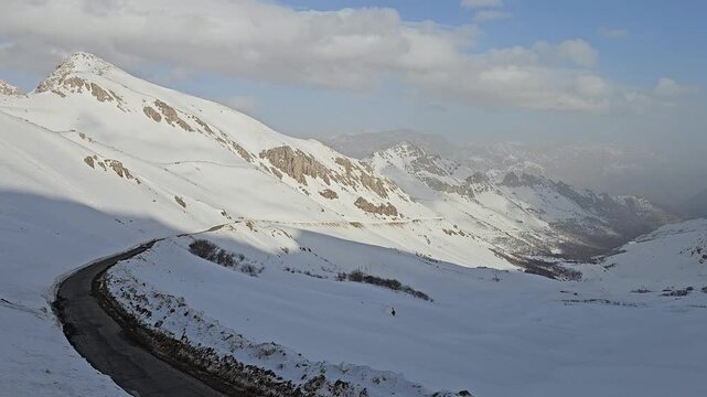 Winding mountain road curves dramatically through deep snow into a vast misty valley surrounded by rugged snow-covered peaks under dramatic cloudy sky.
📍Hawraman Takht, Kurdistan 