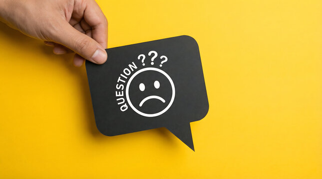 Hand holding black speech bubble with sad face and question marks, yellow background.