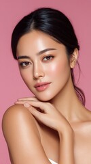 Portrait of an Asian female model softly pressing her jawline with a subtle blush against a pink background