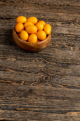 small orange fruits of juicy fresh and fragrant kumquat on a black wooden table, oval oblong kumquat fruit scattered on a black table made of pine