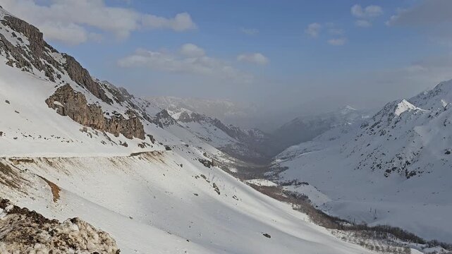 Epic winter mountain valley: snow-draped rugged slopes and distant misty peaks under vast blue sky with scattered clouds in breathtaking high-altitude wilderness.
📍Hawraman Takht, Kurdistan 