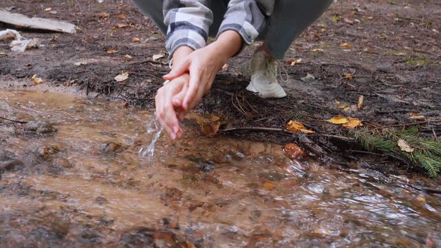 Crouching woman washing her hands in the clean, running water of a small stream in an autumn forest, enjoying a refreshing moment in nature and connecting with the natural environment
