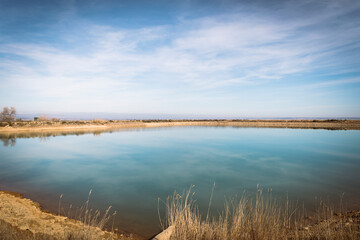 Obraz premium Minimal landscape of calm blue lake under soft sky with distant horizon. Serene natural water reservoir reflecting light in open rural environment with wide copy space.