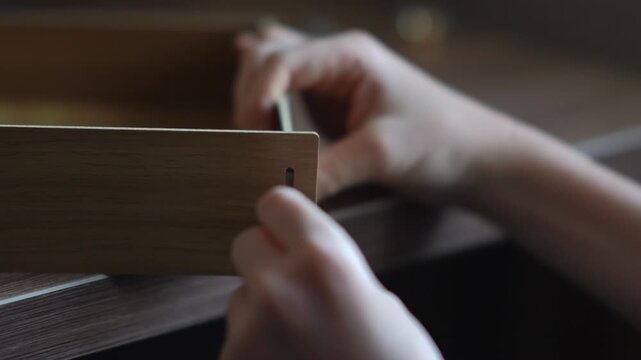 teenager assembling a shelf. A teenager assembles a bookshelf. The child tries on the parts to assemble the furniture. Inserts a screw into the hole and tightens the parts