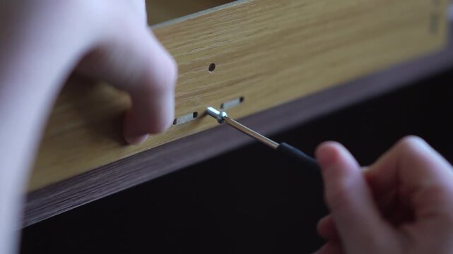 teenager assembling a shelf.  A teenager assembles a bookshelf. The child tries on the parts to assemble the furniture. Inserts a screw into the hole and tightens the parts