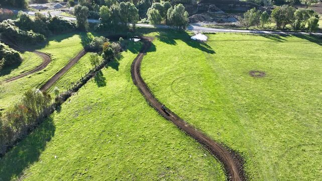 Aerial view of an enduro rider navigating a winding dirt track in a vibrant green field, captured by a drone tracking the movement from above.