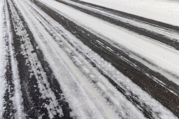 details of an asphalt road with car ruts and part of the road completely covered with ice and snow, part of the road for cars in snow and ice after snowfalls and road treatment with salt
