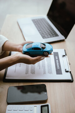 A woman reviews and signs a car insurance policy at her desk with a calculator, laptop, and miniature cars, representing auto coverage planning and financial protection.