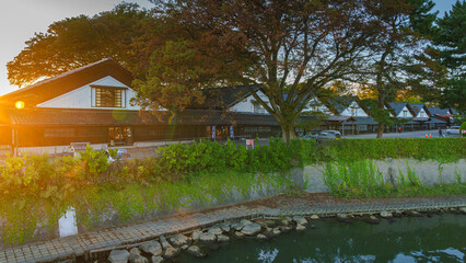 Obraz premium Sakata, Yamagata, japan - Oct 5 2024, Panoramic view from water of Sankyo Soko Storehouse with an alley of trees nearby, at sunset, without people, Sakata, Japan