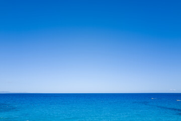 Fototapeta premium Minimalist seascape with a vibrant blue sky meeting the tranquil turquoise waters of the Mediterranean near Baunei, Sardinia. The horizon is crisp and the scene radiates serenity and openness.