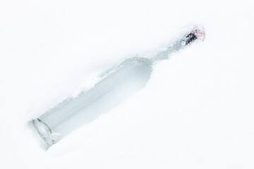 A transparent glass bottle in the fluffy, white snow. Chilled alcohol concept.