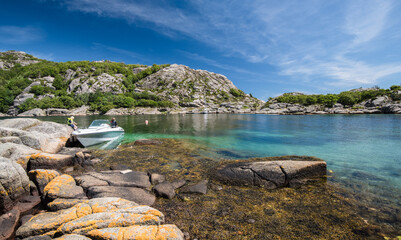 Small motorboat anchored in rocky coastal bay under blue sky. © Trygve