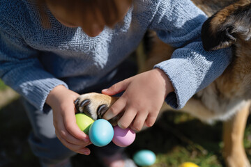 A young child is joyfully collecting colorful Easter eggs with a dog nearby, showcasing the vibrant atmosphere of Easter celebration and the bond between children and pets.