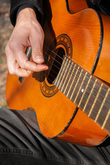 Fototapeta premium Close up hands of playing string guitar outdoors in autumn forest. Concept of sound therapy, mental health and wellness rituals. Calmness tranquility audio-sensory practices. Aura farming energy