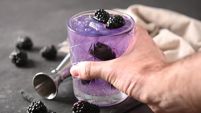 Hand holding bramble cocktail with blackberries and crushed Ice on black background
