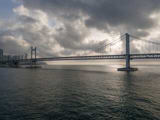 Obraz premium Busan, South Korea, February 22, 2026 Gwangan Bridge sea bridge at sunrise over calm ocean water. Storm Clouds and Moody Weather above coastal city skyline creating a Cinematic Background.